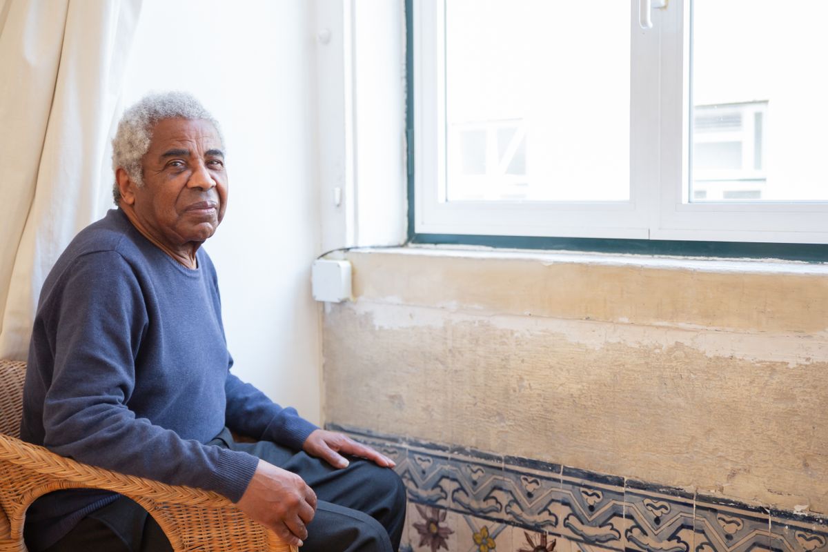 An older man sitting independently by a window at home